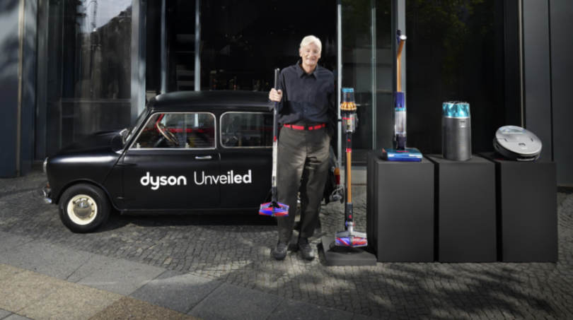 Man standing by a black car and Dyson products.