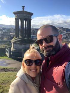 Selfie of a couple in Edinburgh, Scotland, with a monument in the background.