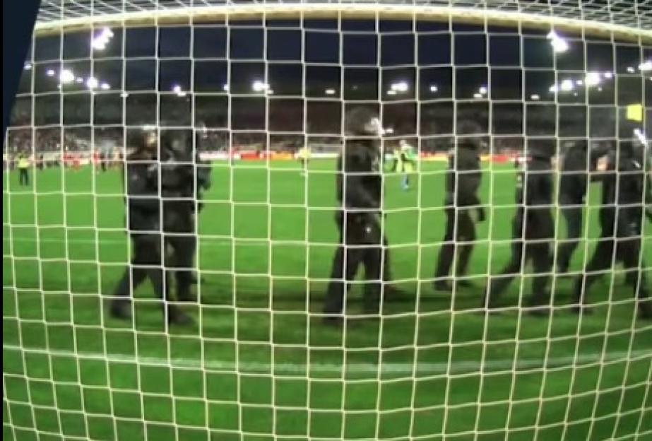 Police officers walking across a soccer field behind a goal.