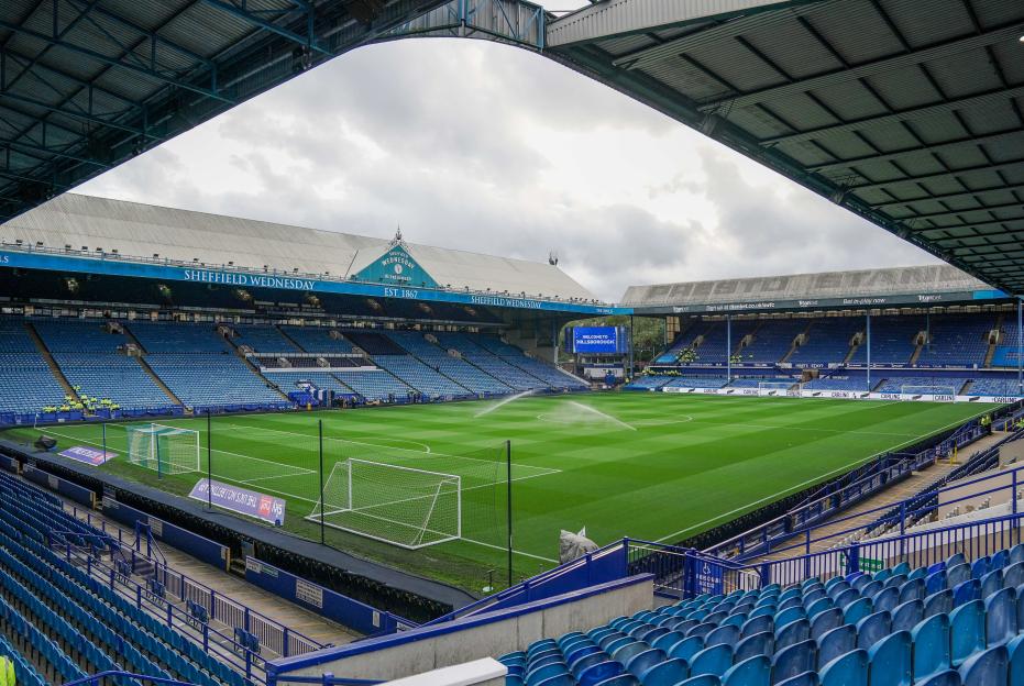 General view inside Hillsborough Stadium with rows of empty blue seats, a green football pitch, and a scoreboard that reads "WELCOME TO HILLSBOROUGH."