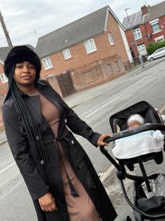 A woman pushes a stroller while looking at the camera.