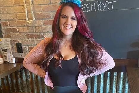 Photo of a young woman with long red hair wearing a pink cardigan and black top.