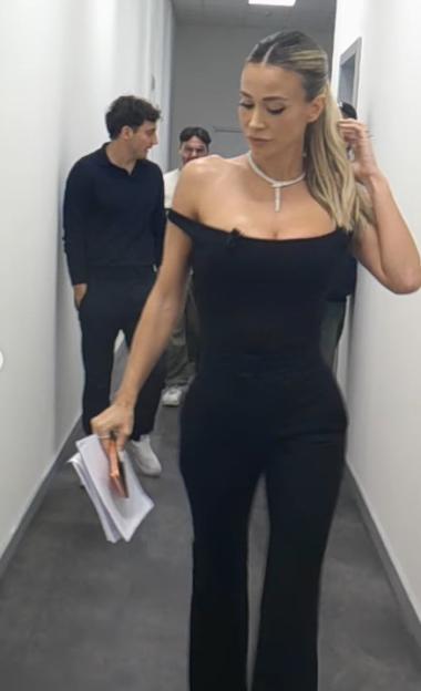 Diletta Leotta walking down a hallway in a black jumpsuit and diamond necklace.