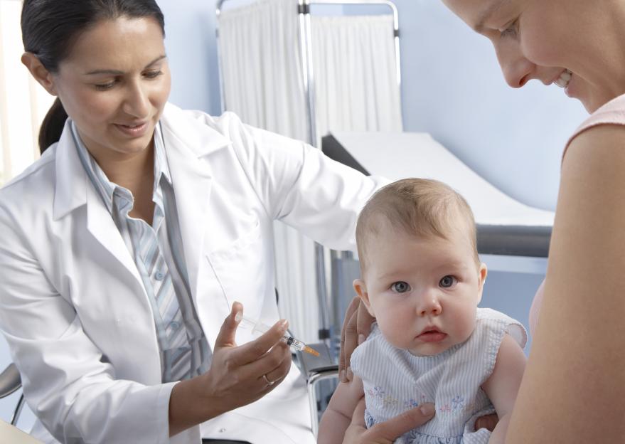 A doctor preparing to give a vaccination to a 5-month-old baby held by an adult.