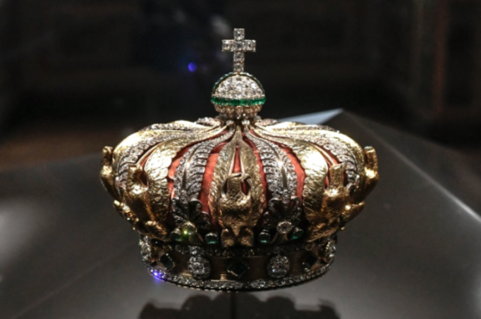 Gold crown adorned with diamonds and emeralds, with a cross on top.