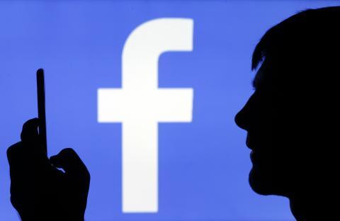 Silhouette of person using phone in front of Facebook logo.