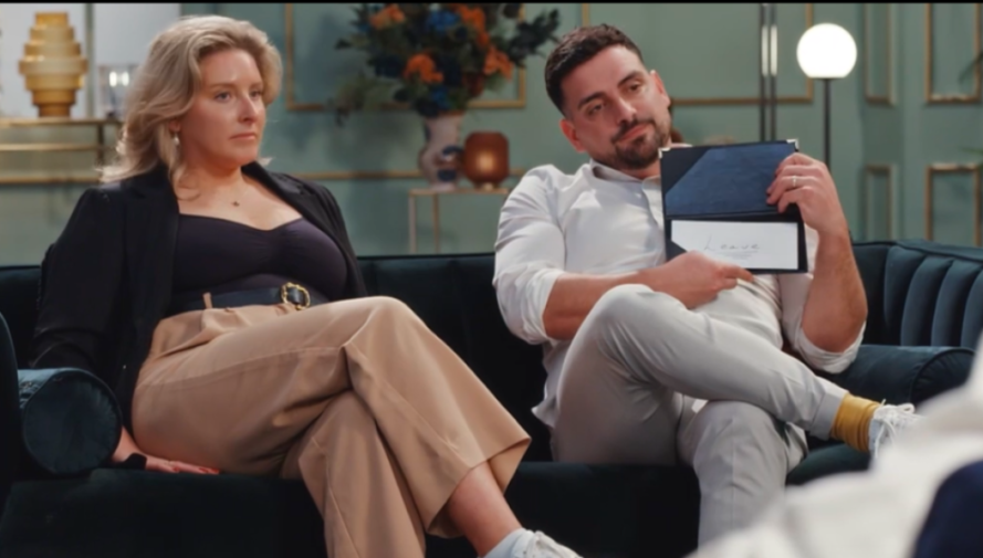 Emma and Caspar sitting on a couch, with Caspar holding up a card that says 'Leave.'