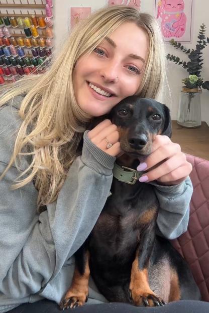 Lucy Bowes smiling while hugging her black and brown dachshund.