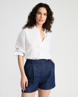 Woman wearing navy linen-blend pleated shorts and a white linen shirt.