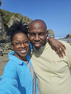 Jacqueline Shepherd and David Gorgeous, a couple, smiling for a photo at the beach.