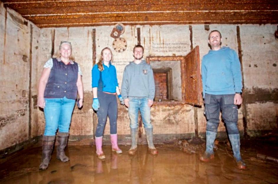 Four people standing in a flooded WWII-era Nazi bunker.