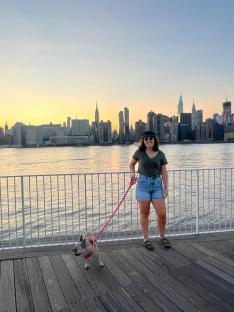 Woman walking a dog with the NYC skyline in the background.