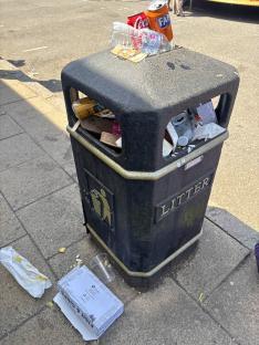 Overfilled litter bin with discarded food and drink containers.
