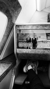 Black and white photo of feet up on an Emirates airplane seat with the in-flight entertainment screen visible.