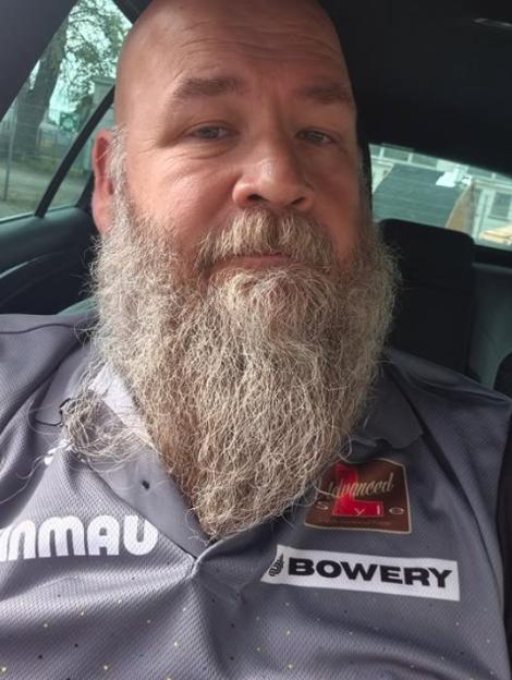 Man with a long grey beard wearing a grey polo shirt with the words "BOWERTY" and "Advanced Style" on it.