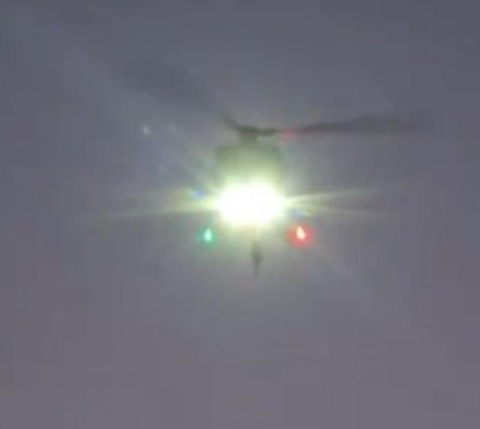 A helicopter flying at night with bright lights.
