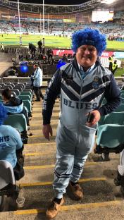 Man in NSW Blues onesie at a stadium.