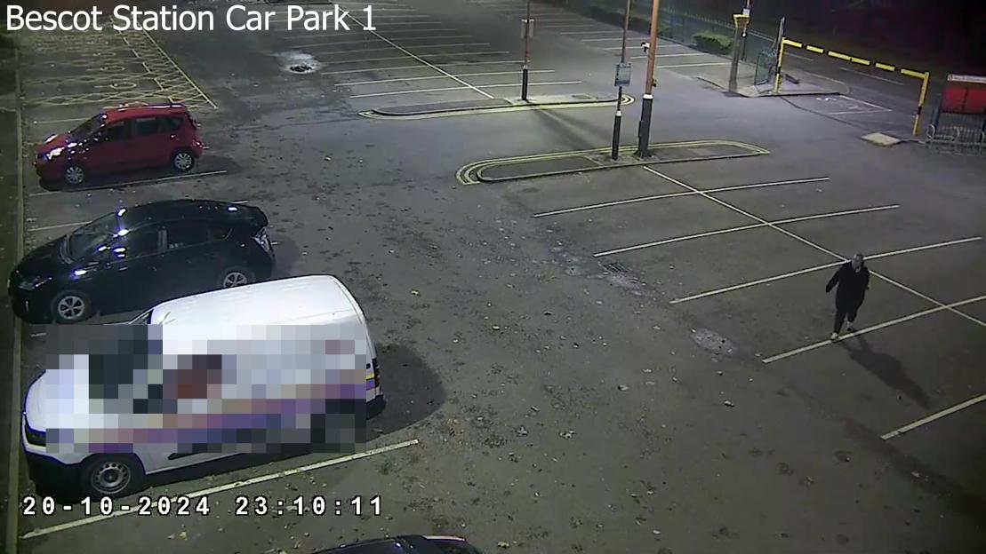 CCTV footage of a car park with parked vehicles and a person walking.