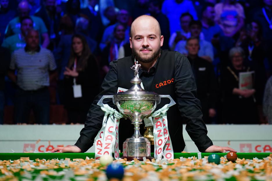 Snooker player Luca Brecel with the trophy on a table covered in confetti.