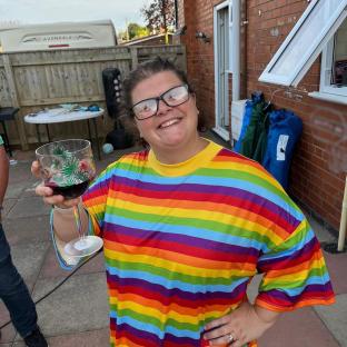 Woman in rainbow shirt holding a glass of wine in her garden.