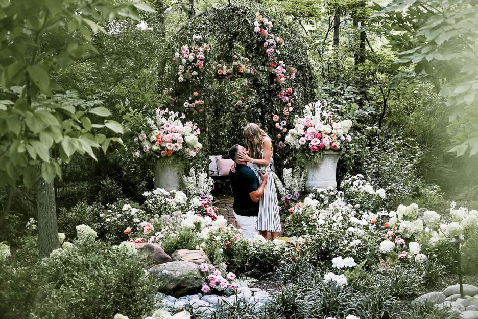 A man proposing to a woman in a flower-filled garden.