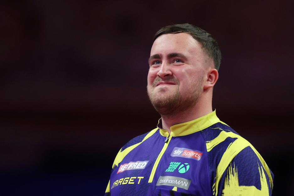 Luke Littler of England smiling during a darts match.