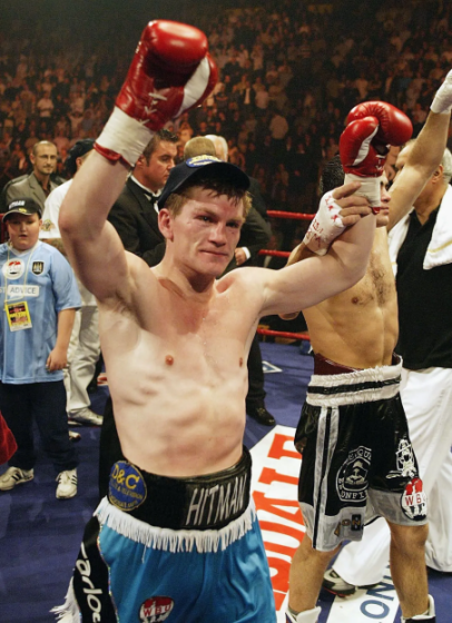 Boxer Ricky Hatton raises his gloved hands in victory while standing next to another boxer.