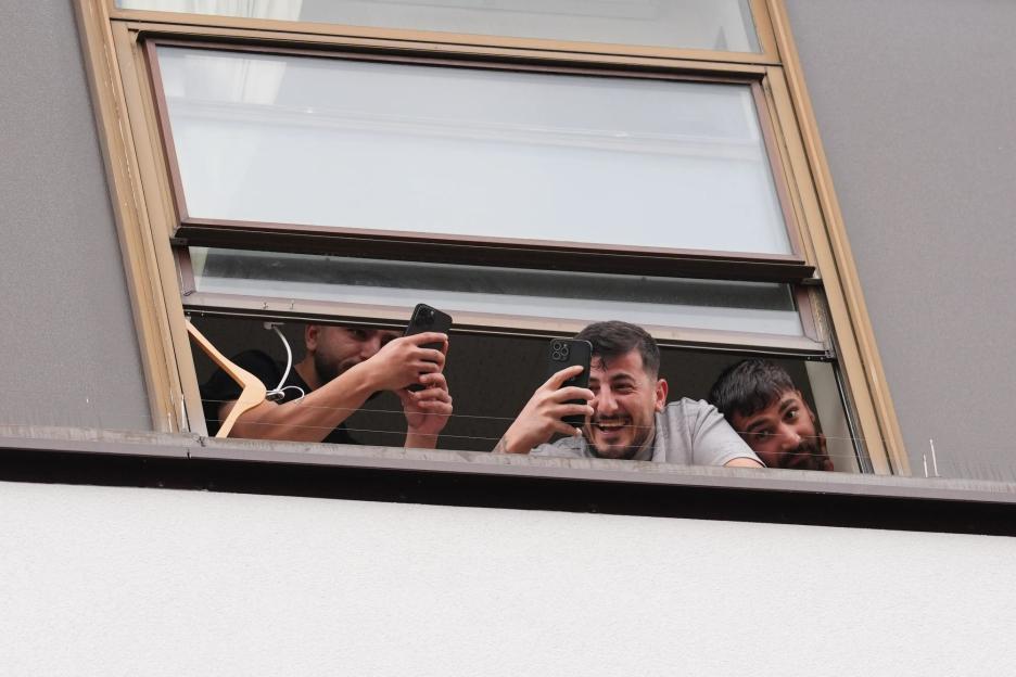 Migrants blow kisses from hotel window as they film protesters clashing with police on streets below