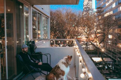 Man and dog on a balcony at night, city lights in the background.