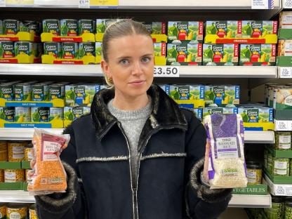 Woman in a grocery store holding bags of lentils and rice.