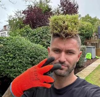 Man with turf on his head wearing gardening gloves.