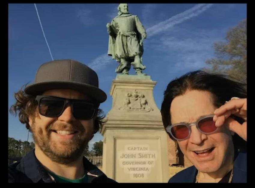 Photo of two men smiling in front of a statue of Captain John Smith.