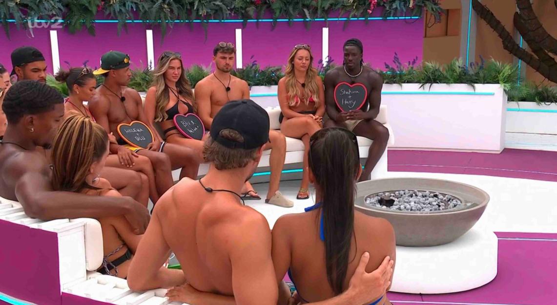 Love Island couples holding heart-shaped signs.