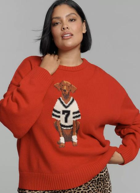 A woman wearing an orange sweater with a dog in a football jersey.