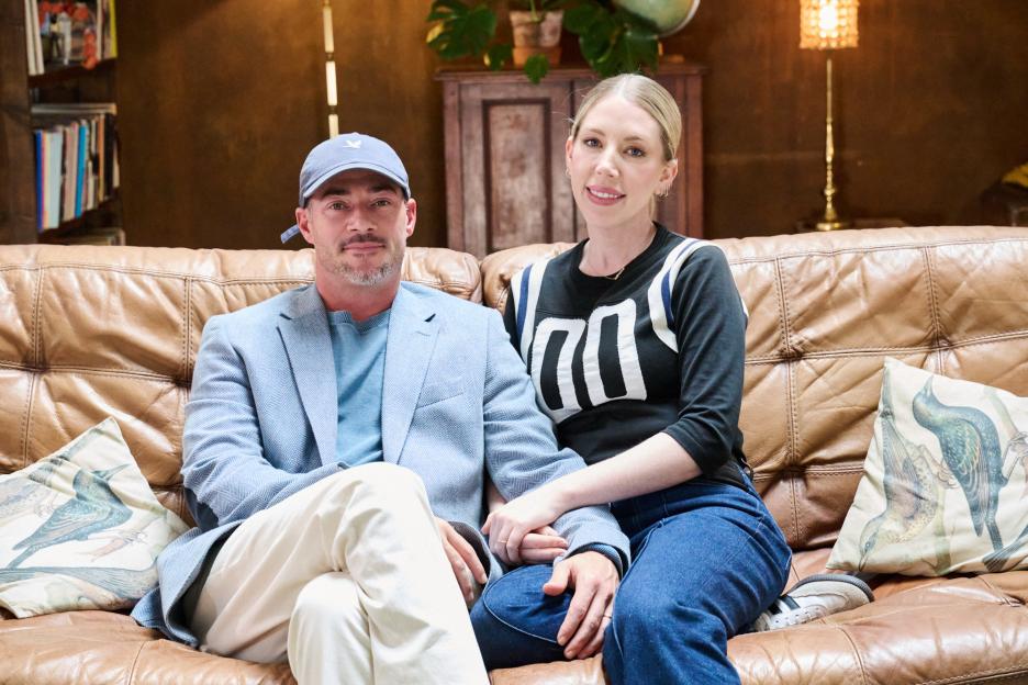Katherine Ryan and Bobby Kootstra sitting on a brown leather couch.