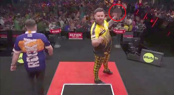 A darts player gives the middle finger to a spectator.