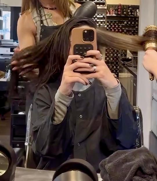 Woman taking a selfie while getting her hair styled at a salon.