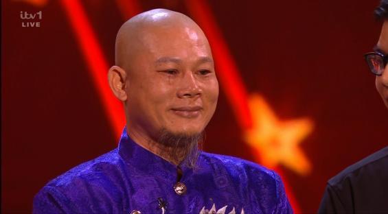 Screenshot of a man in a purple shirt, appearing emotional.