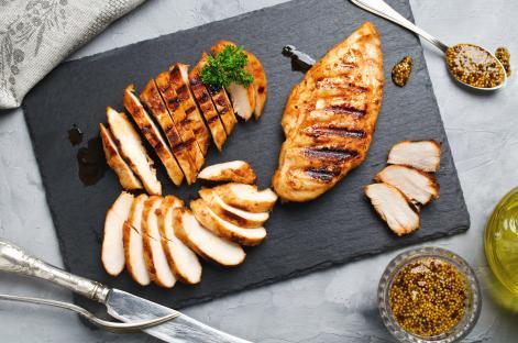 Grilled chicken fillets sliced on a slate plate with mustard.