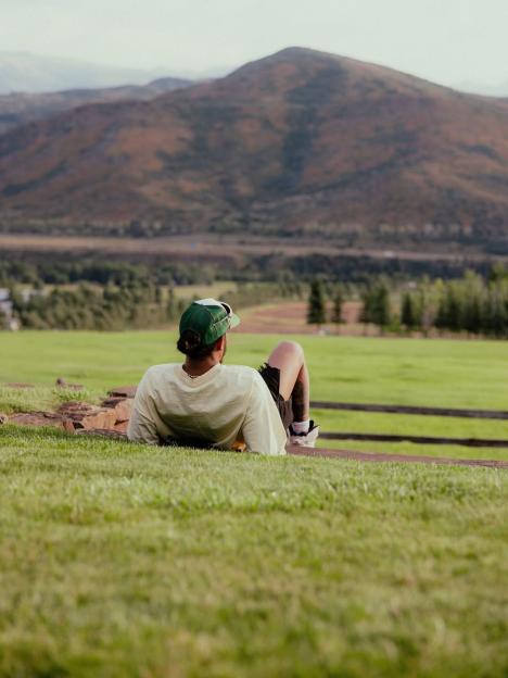 Person relaxing on grassy hill overlooking mountains.