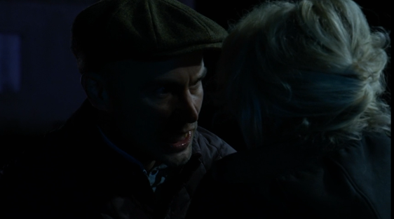 A man in a cap confronts a woman in the dark.