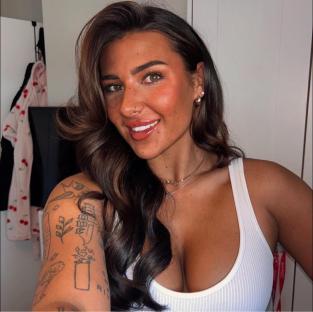 Close-up selfie of a woman with long brown hair and tattoos.
