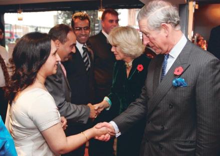 King Charles III shaking hands with a woman, Camilla, Duchess of Cornwall, and other people nearby.