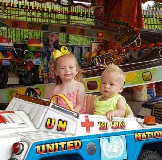 Two young children in a toy car decorated with United Nations and Red Cross logos.