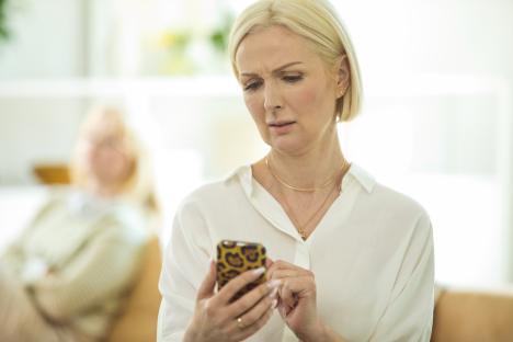 Worried woman looking at her phone with a teenager in the background.