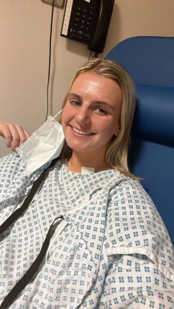 Woman in hospital gown holding a face mask.
