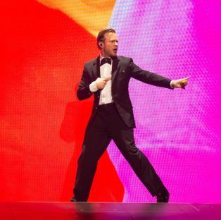Olly Murs performing on stage with a large screen displaying a stylized image of himself.
