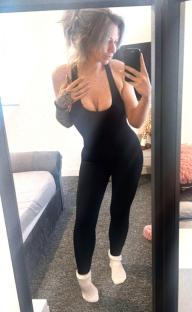 Woman in black jumpsuit taking a selfie in a mirror.
