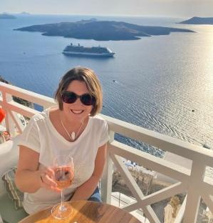 Woman enjoying a glass of rose wine on a balcony overlooking the ocean and a cruise ship.
