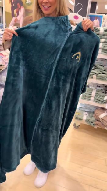 A woman holding up a dark teal plush wearable blanket with a gold Star Trek insignia.